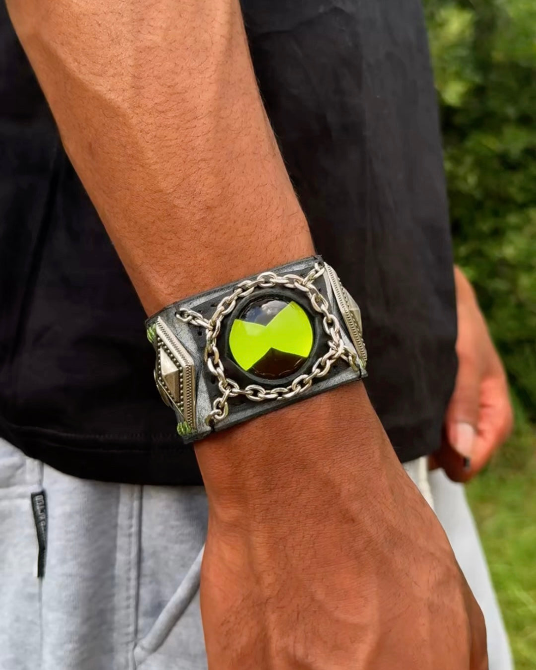 A green ben 10 omnitrix bracelet wear by a man wearing a black t-shirt.