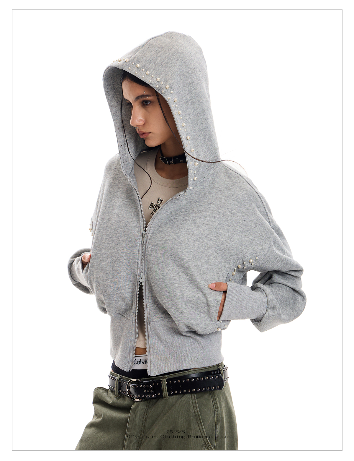 A person with long dark hair models a gray studded Street Hoodie, with the hood up, over a light-colored top.