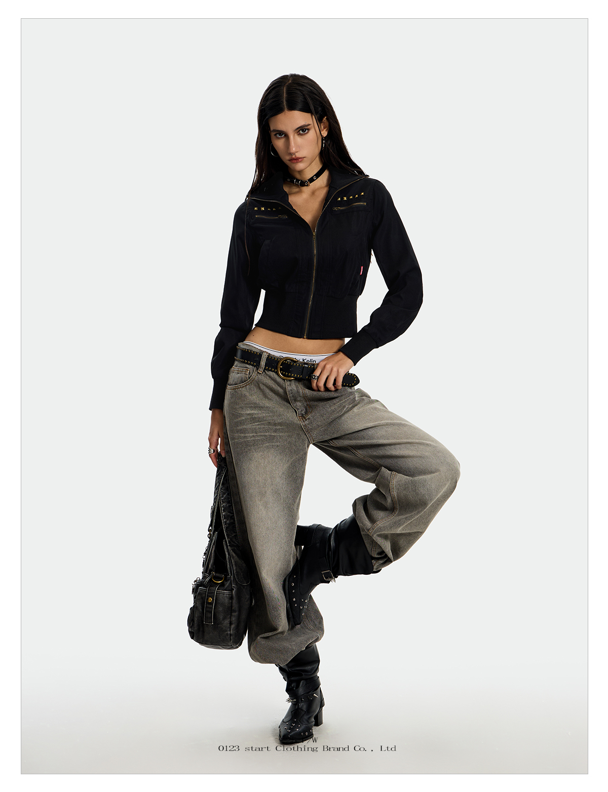 A young woman modeling an UrbanRebel Camo Jacket with a matching black skirt, knee-high boots, and a black purse.