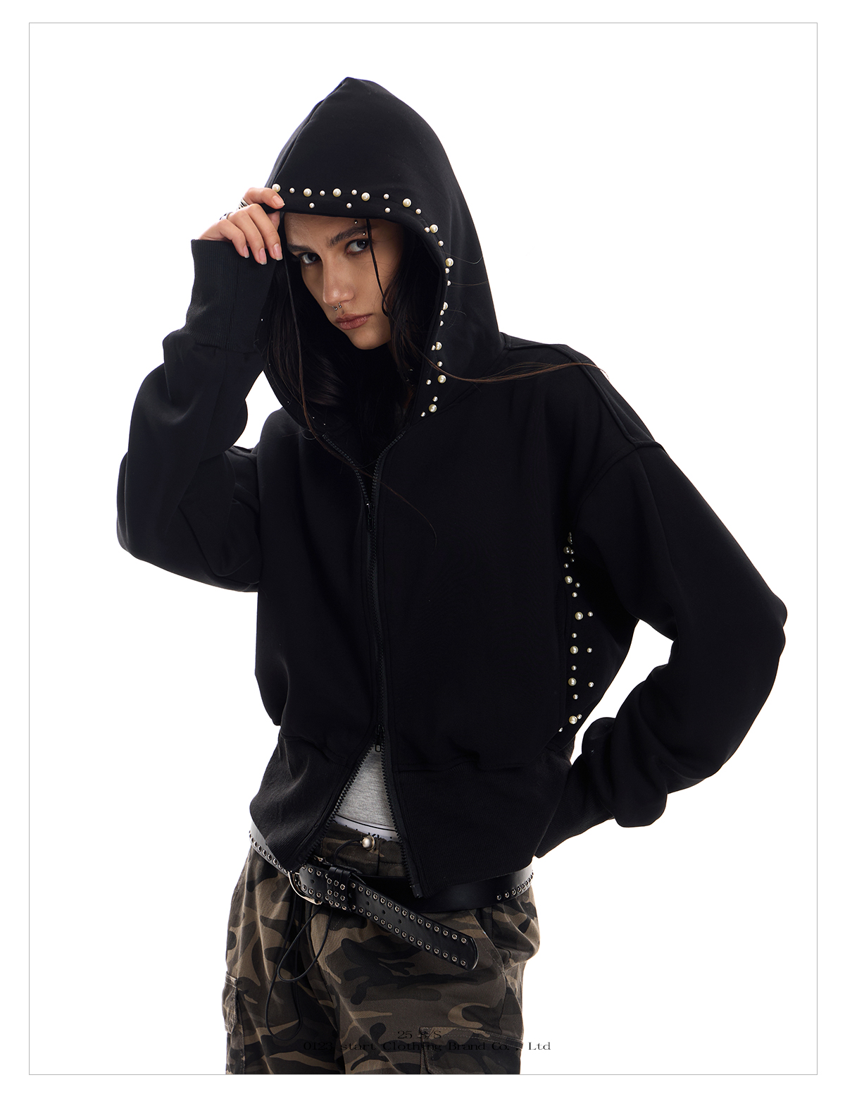 A full-length shot of a young woman posing in a black Street Wolf Hoodie with pearl and stud detailing on the hood and sides.