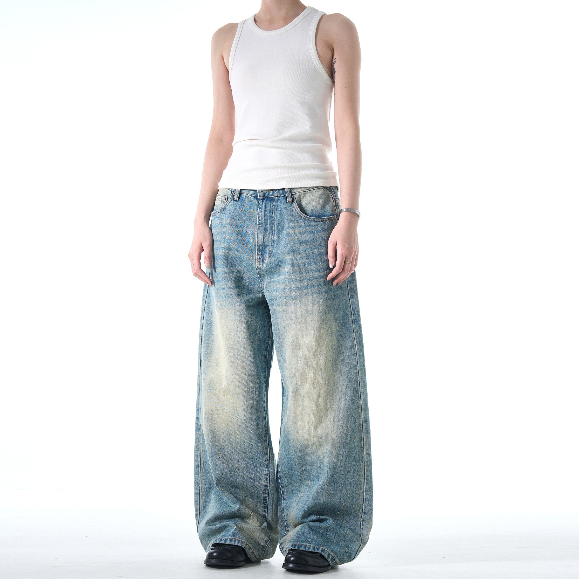 A person stands wearing a white tank top and black shoes, modeling a pair of loose-fitting Retro Washed Design Cleanfit Jeans with a light, faded wash.