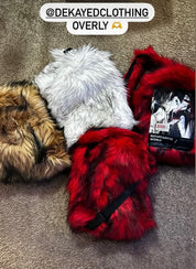 An overhead view of four fluffy Plush Backpacks - Lost Series in brown, white, and two shades of red are shown lying on a carpeted floor.