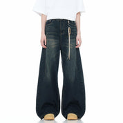 A pair of dark-wash, baggy denim jeans are worn by a person standing with their feet slightly apart, showing the wide leg opening and distressed texture.