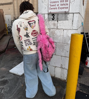 A person wears a cream-colored hoodie and light baggy jeans carries a hot pink Plush Backpacks - Lost Series over one shoulder, adding a playful touch.