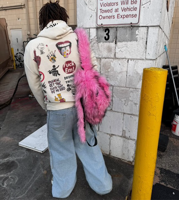 A person wears a cream-colored hoodie and light baggy jeans carries a hot pink Plush Backpacks - Lost Series over one shoulder, adding a playful touch.