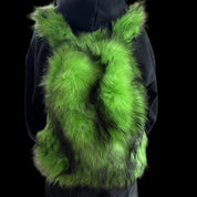 A fluffy, vibrant green Plush Backpacks - Lost Series with hints of dark fur is worn on a person's back, set against a dark background.