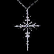 A dazzling WHITE GOLD APOSTLE NECKLACE pendant, featuring an intricate, diamond-encrusted cross design with a central gem, hangs from a rope chain against a dark background.