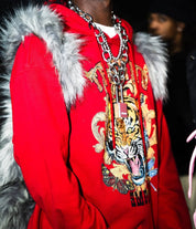 A person wears a vibrant red hoodie with a detailed tiger and ornate gold embroidery, layered with multiple chunky silver chains and a grey furry Plush Backpacks - Lost Series or similar accessory on their back.