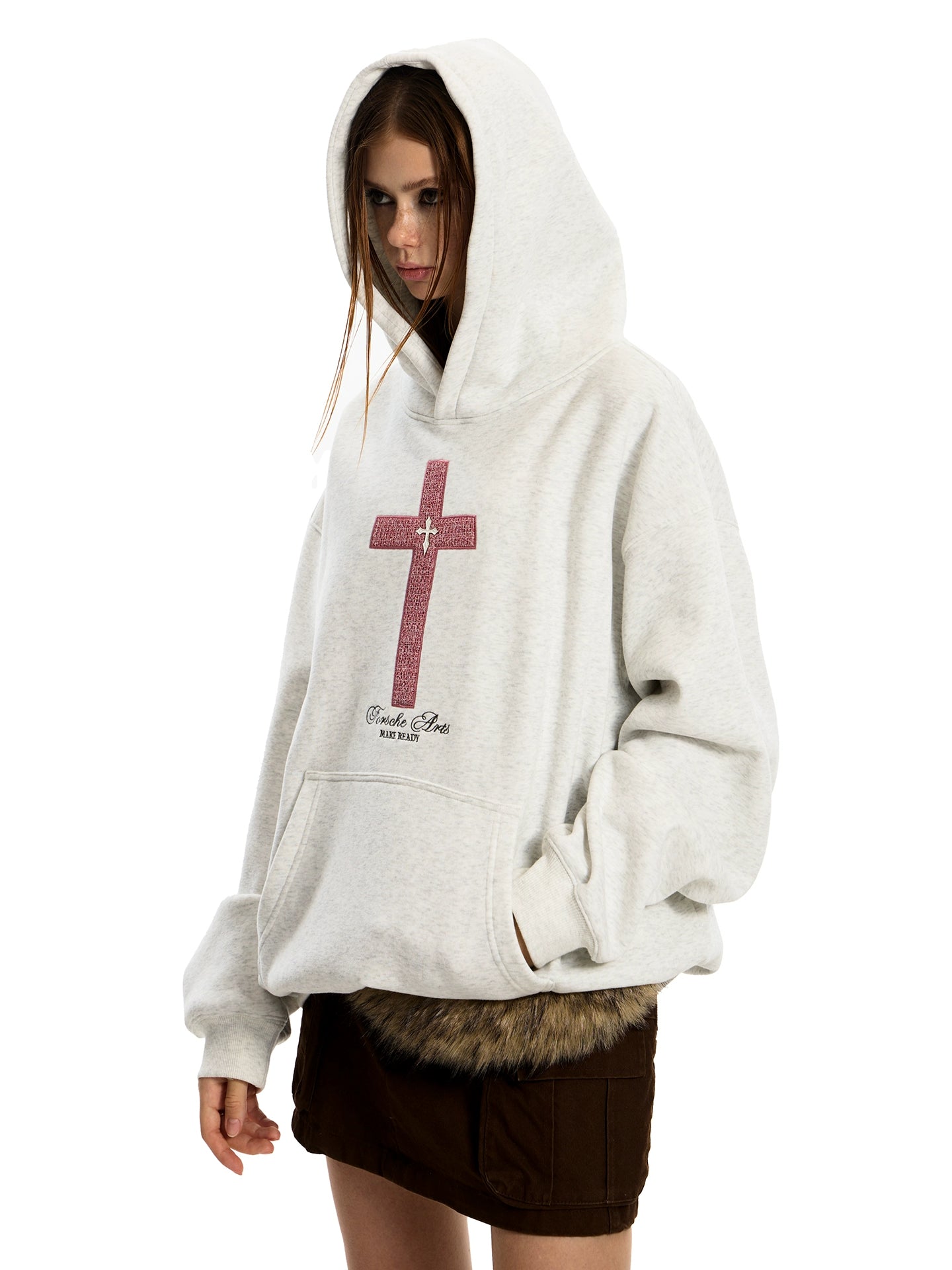 A woman models an oversized, light gray GOTHIC HOODIE with a prominent red cross graphic holding his pocket.