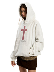 A woman models an oversized, light gray GOTHIC HOODIE with a prominent red cross graphic holding his pocket.