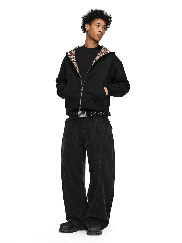 A person with dark, curly hair poses with their hands in the pockets of a black Leopard Lined Jacket, which is unzipped to reveal a black shirt.