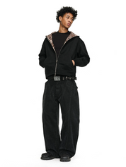 A person with dark, curly hair poses with their hands in the pockets of a black Leopard Lined Jacket, which is unzipped to reveal a black shirt.