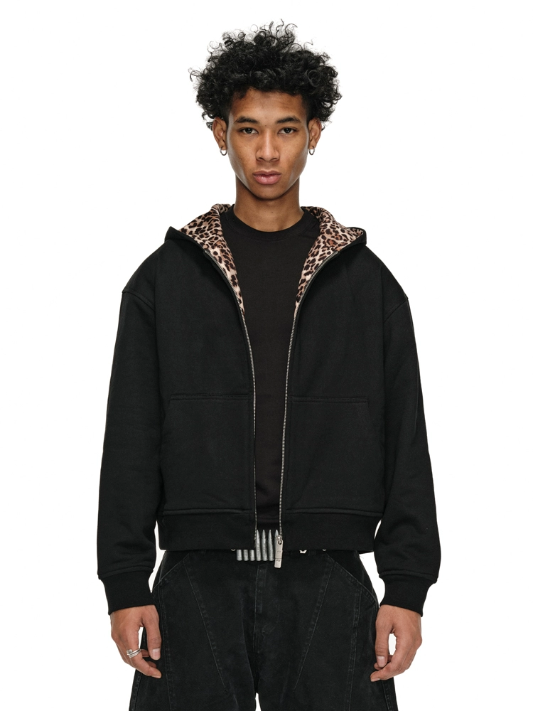 A person with dark, curly hair models a black Leopard Lined Jacket with the hood up.
