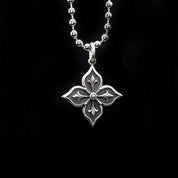 A detailed, silver melody necklace with a floret-shaped pendant hangs against a solid black background.