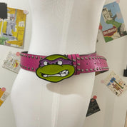 A pink studded ninja turtle belt with a large Donatello face as the buckle is shown worn on a white mannequin against a background of various posters and artwork.
