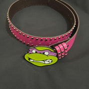 A bright pink belt, adorned with silver studs, features a prominent ninja turtles belt buckle depicting Donatello's face.