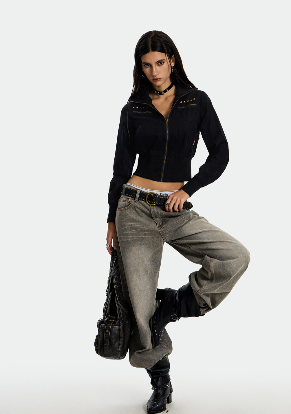 A young woman modeling an UrbanRebel Camo Jacket with a matching black skirt, knee-high boots, and a black purse. 