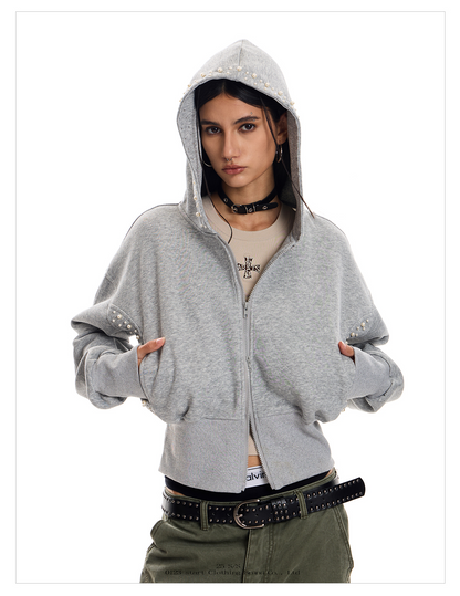 A person with dark hair wears a gray studded Street Hoodie with the hood up, over a light-colored top. 