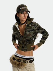 A full-length shot of a young woman posing while wearing an UrbanRebel Camo Jacket with a matching baseball cap, tan pants, and a furry fanny pack.