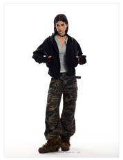 A woman models a black Street Wolf Hoodie with silver stud detailing on the sleeves and hood. She is also wearing a gray shirt, camouflage pants, and furry brown boots.