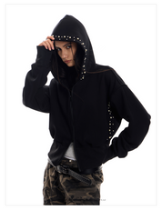 A full-length shot of a young woman posing in a black Street Wolf Hoodie with pearl and stud detailing on the hood and sides.