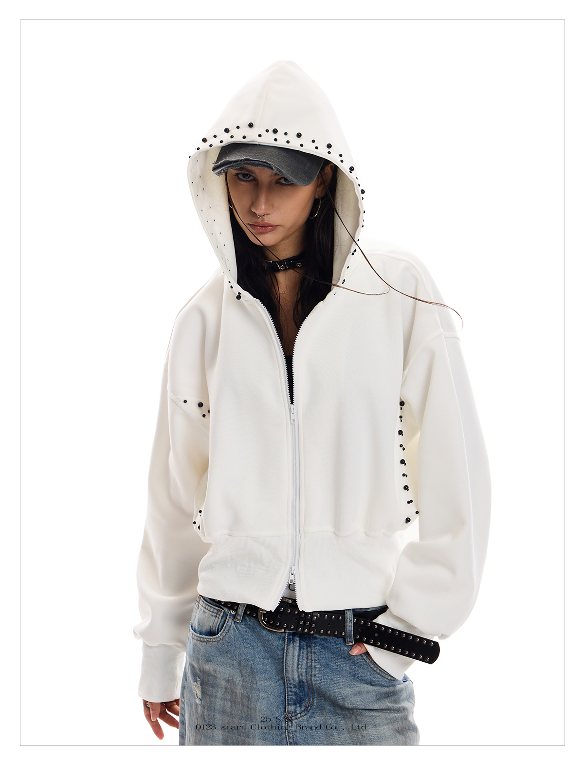 A person with dark hair wears a white Wolf Street Hoodie with black stud detailing on the sleeves and hood.