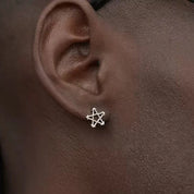 Close-up of a person wearing a ABYSS" STAR EARRINGS on the left ear.