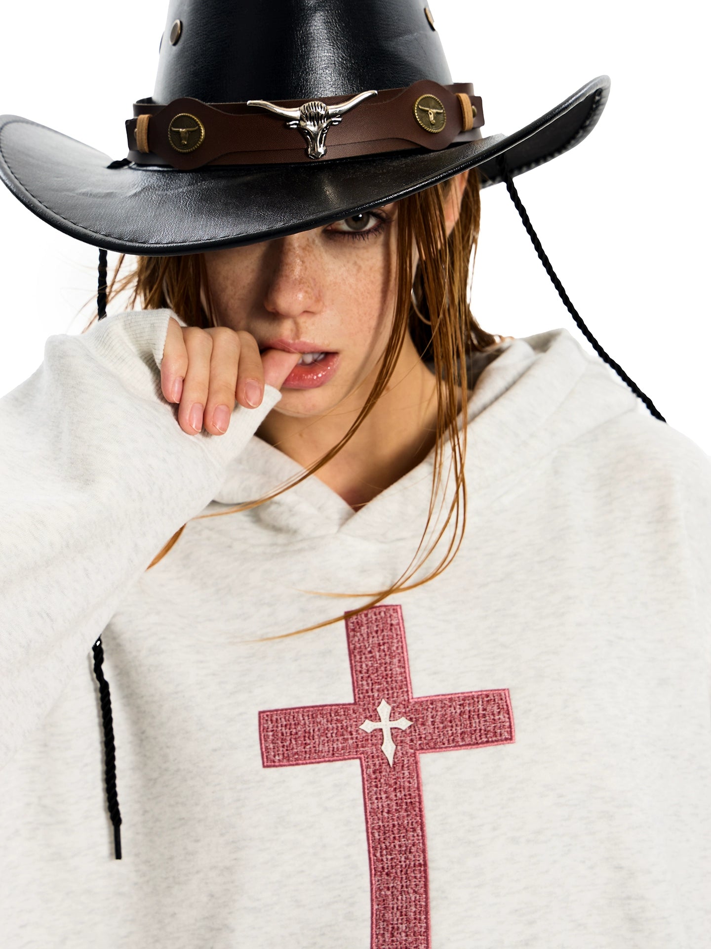 A woman suggestively biting her finger while wearing a light grey GOTHIC HOODIE for WOMEN with a red cross design.