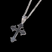 A polished silver cross pendant, with a design similar to the MICRO DIAMOND CROSS NECKLACE but without diamonds, hangs from a Cuban link chain against a dark background.