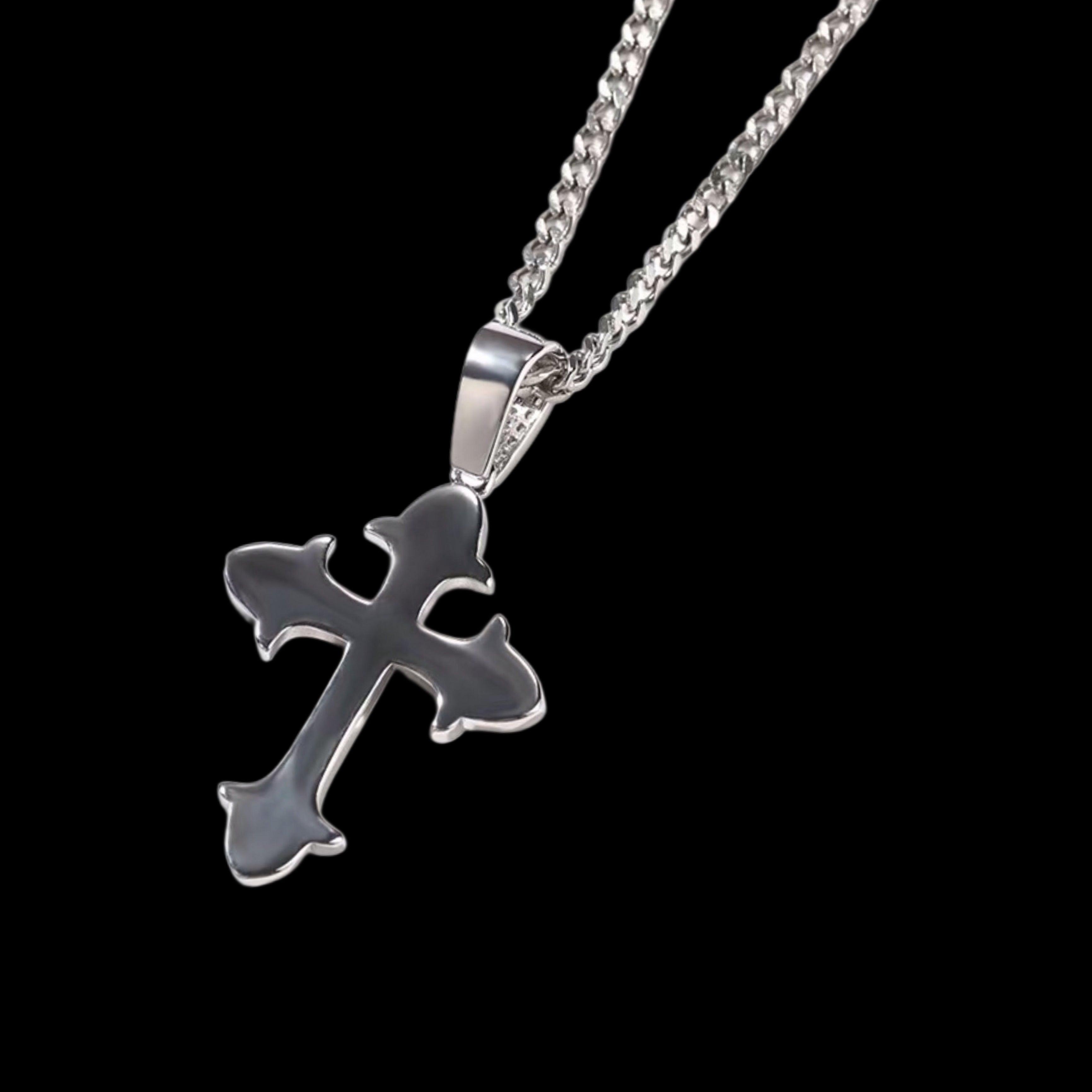 A polished silver cross pendant, with a design similar to the MICRO DIAMOND CROSS NECKLACE but without diamonds, hangs from a Cuban link chain against a dark background.