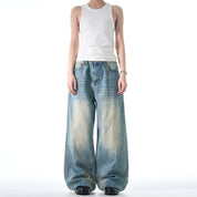 A person wearing a white tank top and black shoes models a pair of Retro Washed Jeans that are loose and wide-legged.