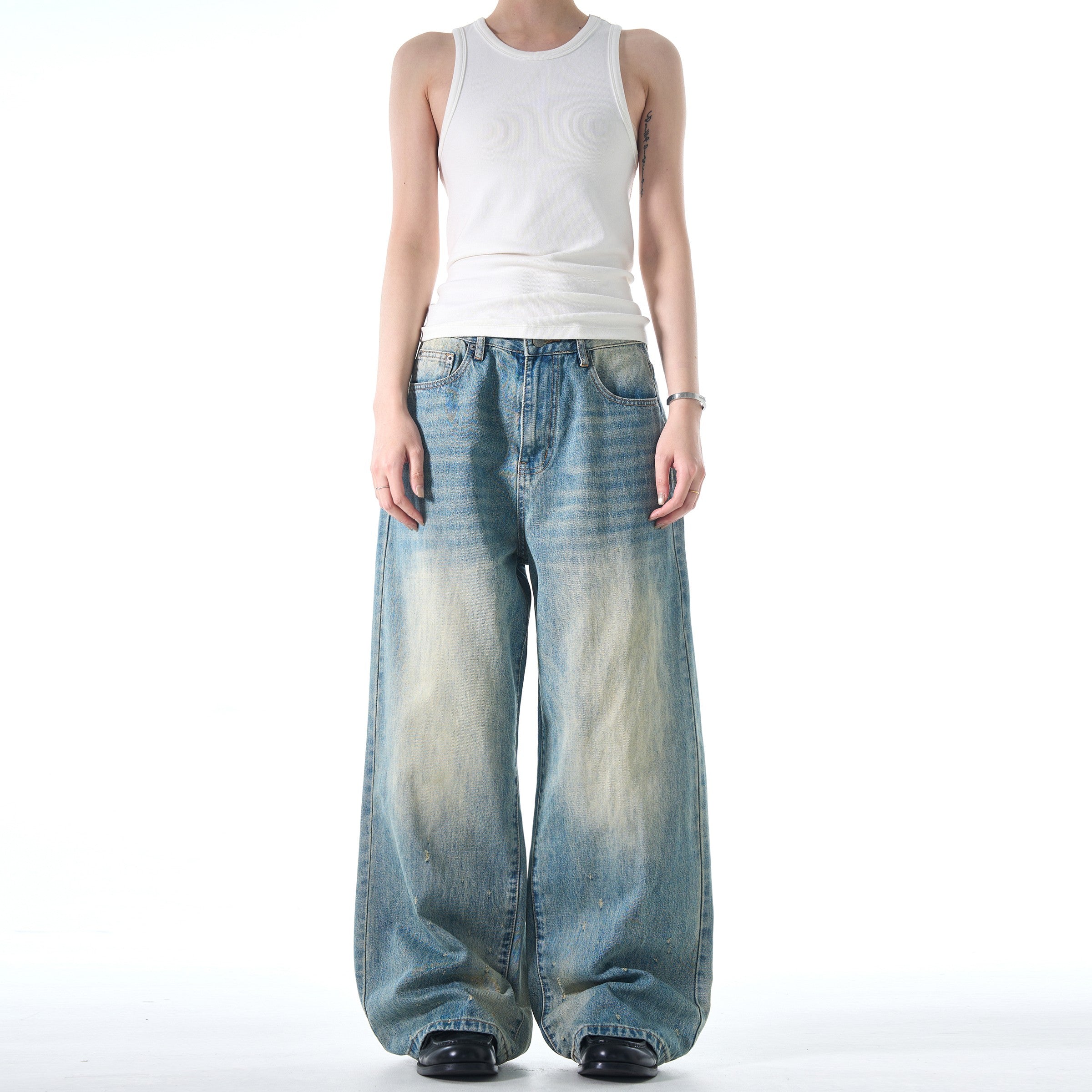 A person wearing a white tank top and black shoes models a pair of Retro Washed Jeans that are loose and wide-legged.