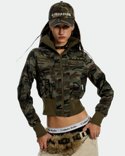 A young woman wearing an UrbanRebel Camo Jacket with a matching baseball cap, tan pants, and a furry fanny pack.