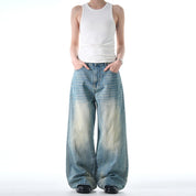 A person stands with hands in their pockets, wearing a white tank top and black shoes with a pair of loose, wide-legged Retro Jeans.
