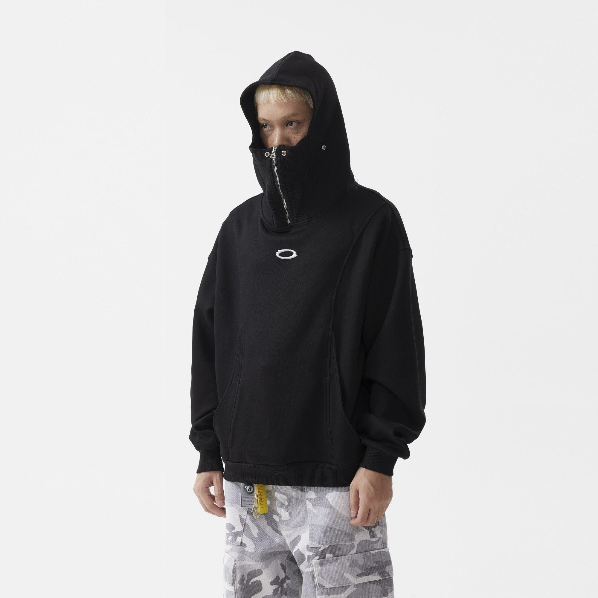 A male model wears a black masked hoodie with a zipper going up the center.