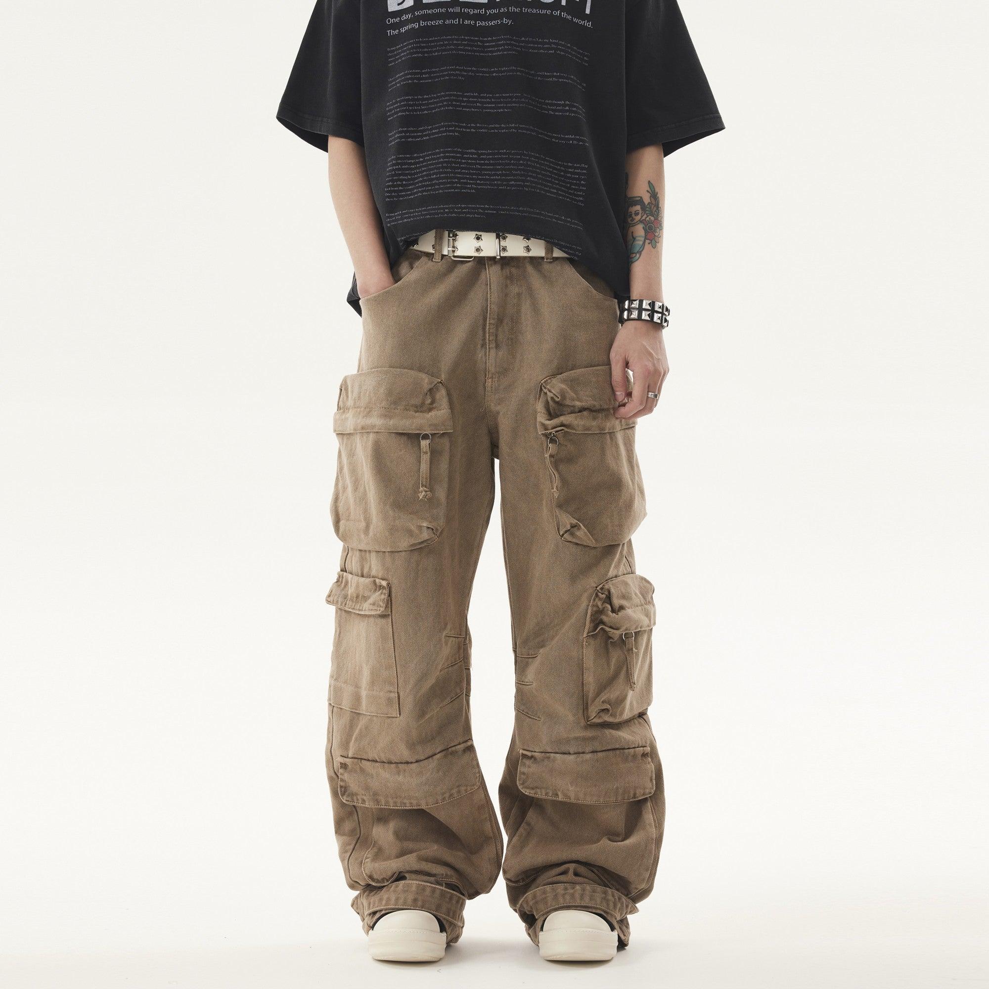A person stands wearing a black t-shirt and light brown Heavy duty Vibe Cargo Jeans with multiple large pockets, accessorized with a studded white belt and bracelet.