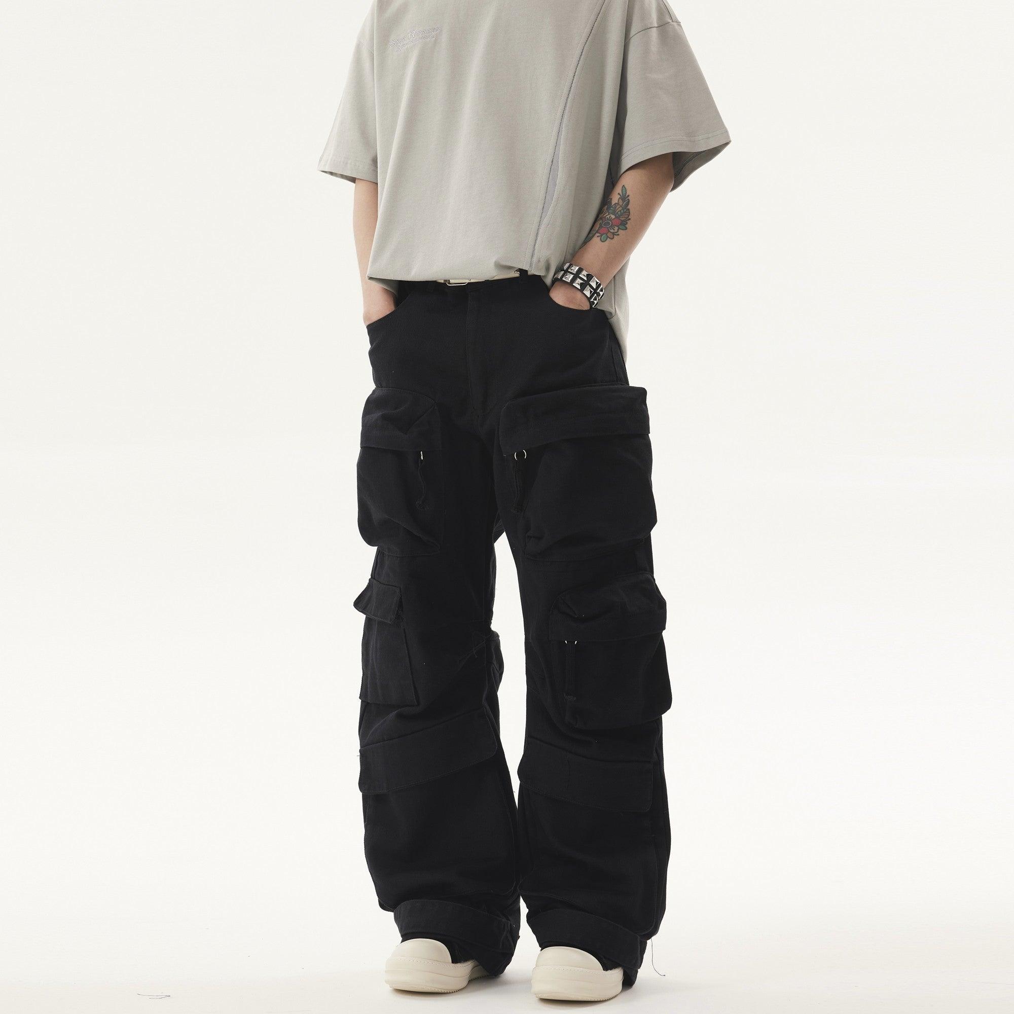 A person stands wearing a light grey t-shirt and black Heavy duty Vibe Cargo Jeans with multiple large pockets, accessorized with a studded bracelet.