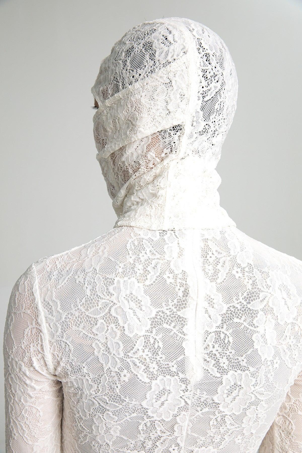 From the back, a person is seen wearing a semi-sheer white lace top with a matching lace hood mask that wraps around their head and face.