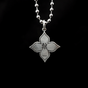 The back of a silver Melody Necklace pendant, which is a floret shape, is shown on a black background, revealing an engraved "N" and "S925" stamp.