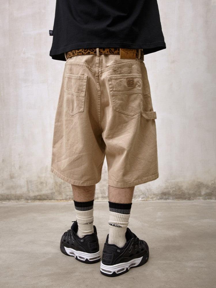 A person is shown from behind, wearing Remedy Straight Workwear Mid-Length Jorts in a khaki color, accessorized with a leopard print belt and paired with a black T-shirt and black sneakers with white striped socks.