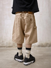 A person is shown from behind, wearing Remedy Straight Workwear Mid-Length Jorts in a khaki color, accessorized with a leopard print belt and paired with a black T-shirt and black sneakers with white striped socks.