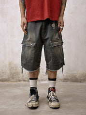 A person stands wearing distressed and frayed Remedy Washed Tassel Workwear Jorts with large cargo pockets, paired with a faded red T-shirt and dirty sneakers with white socks.