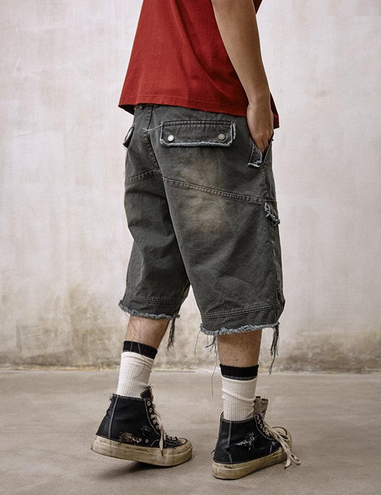 A person is shown from behind wearing a red t-shirt and Remedy Washed Tassel Workwear Jorts with large back pockets and a frayed, distressed hem, paired with dirty high-top sneakers and white and black striped socks.