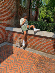 A man sitting with Multi Leopard Print Plush Backpacon the ground.